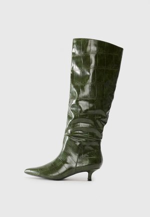 Bota alta de couro verde escuro com padrão de crocodilo, com bico apontado e salto kitten baixo, mostrada de lado num fundo simples.