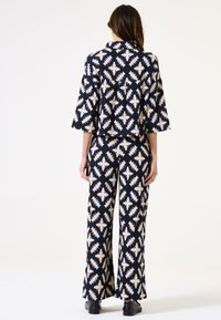 Zweiteiliges Outfit mit einem kurzen Oberteil und weit geschnittenen Hosen aus navyblauem Stoff mit cremefarbenen Zickzackmustern, entworfen mit lockeren Ärmeln.