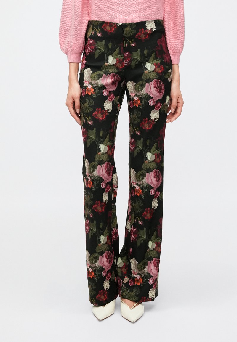Kvetinové nohavice z čiernej látky zdobia veľké ružové a červené ruže, zelené listy a priliehavý pás, ktoré sú skombinované so špicatými bielymi topánkami.