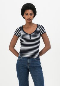 Krátkosleeve, námornícka a biela prúžkovaná ribbed tričko s okrúhlym výstrihom a troch gombíkovou pätou, spojené s modrými džínsami.