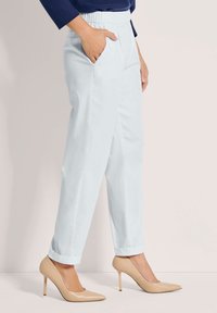 Lichtblauwe broeken met een relaxte pasvorm, voorzien van zijzakken en opgerolde hemden, gecombineerd met nude hoge hakken. Glad stoffen textuur.