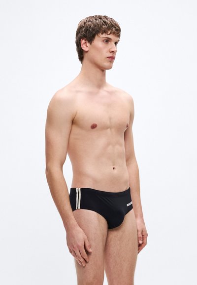 Schwarze Badehose mit zwei vertikalen weißen Streifen an den Seiten und enger Passform. Der Stoff wirkt glatt und elastisch.