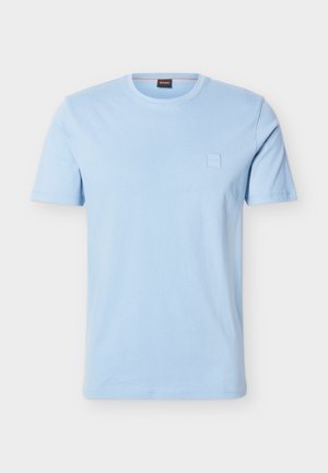 Tricou bleu deschis cu mâneci scurte și gât rotund, cu un mic logo pătrat în relief pe partea stângă a pieptului și o etichetă de gât cu brand.
