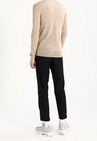 Hellbeiges Langarmhemd, schwarze, schmal zulaufende Hose und hellgraue Sneaker mit weißen Sohlen. Glatte Textur, schlichtes Design und figurbetonte Silhouette.