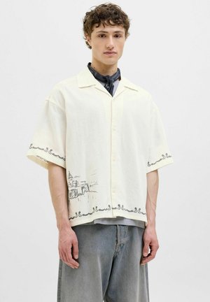 Short-sleeve, cream shirt with a textured fabric, featuring a graphic line drawing along the hem and dark accents on the collar and sleeves.