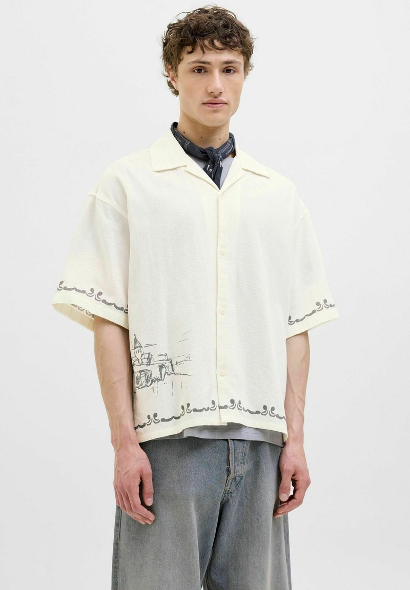 Chemise à manches courtes, crème, en tissu texturé, avec un dessin graphique en ligne le long de l'ourlet et des accents foncés sur le col et les manches.