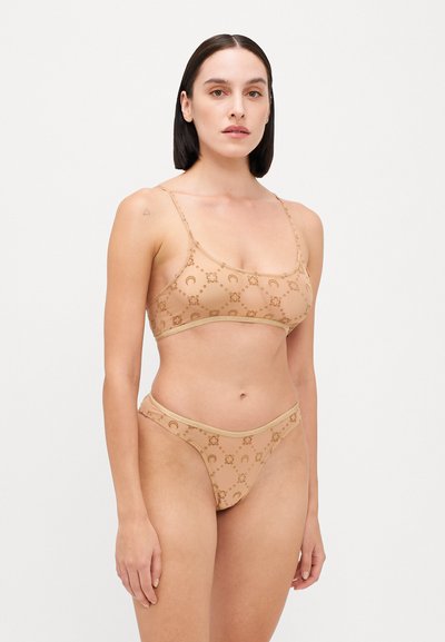 Nude bikini set featuring a bralette top and high-cut briefs. Made of smooth fabric with a circular pattern and subtle gold accents.