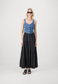 Denim prirezana majica s gumbom, uparena s crnom maksi suknjom s više slojeva. Crne natikače s otvorenim prstima upotpunjuju izgled.