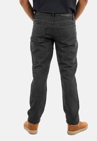 Vaqueros gris oscuro con un corte clásico, que presentan un diseño de cinco bolsillos y detalles de costura sutiles. Combinados con zapatos bajos marrones.
