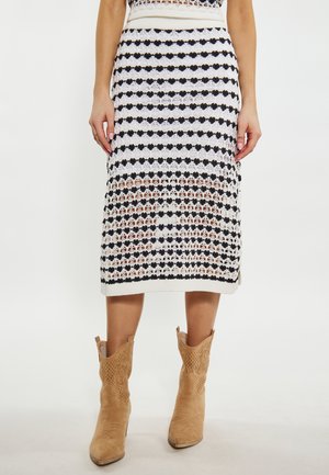 Gebreide midi-rok met afwisselende zwarte en witte patroonen, voorzien van een geribde tailleband. Gekoeld met beige cowboylaarzen.