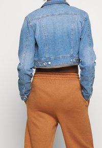 Ljust blå denimkort jacka med klassisk krage, knappdetaljer och långa ärmar. Matchad med bruna avslappnade byxor.