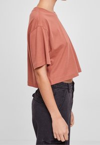 Zkrácený, krátký rukáv tričko v terakotové bavlně, má kulatý výstřih a volný střih, v kombinaci s tmavě šedými kalhotami s vysokým pasem.