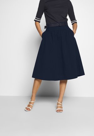 Jupe midi bleu marine avec un design plissé, ceinture en tissu à la taille et poches latérales. Portée avec un haut à rayures à côtes.