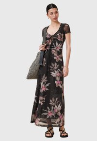 Maxi abito in tessuto nero trasparente con un motivo floreale in rosa e verde. Presenta un corpino aderente con chiusura a fiocco e maniche corte.