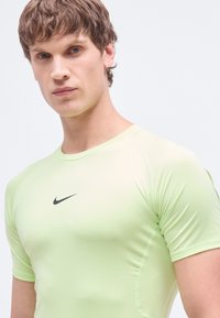 Αθλητική κοντομάνικη πουκαμίσα ανοιχτοπράσινου χρώματος, κατασκευασμένη από λεία, ελαστική ύφανση, με διακριτικό μαύρο λογότυπο Nike στο στήθος.