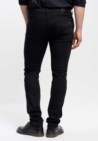 Jeans elásticos negros con corte ajustado, diseño de cinco bolsillos y detalles de costura sutiles. Llevados con botas negras de cordones.