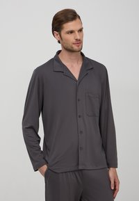 Camicetta da pigiama grigia a maniche lunghe in tessuto morbido, con colletto a punta, bottoni e una tasca sul petto per un ulteriore dettaglio.