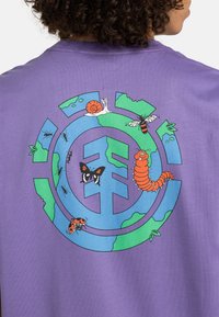 Camiseta de algodón morada con un gráfico colorido de insectos y un caracol dentro de un diseño circular que representa la Tierra.