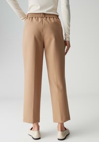 Beige wijde broek met elastische tailleband, voorzien van twee achterzakken, een gladde textuur en een cropped lengte.