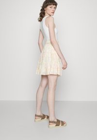 Top branco de alças combinado com uma saia mini em floral pastel com babados e cintura franzida. Sandálias castanhas com tiras e sola creme.