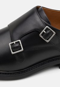 Fekete bőr cipő két ezüstcsattal, sima textúrával, kerek formával és kontrasztos bézs belső résszel. Varrott részletek a talpon.