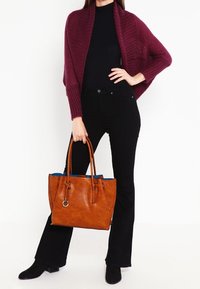 Braune Leder-Shopper-Tasche mit zwei Griffen, einem blauen Innenfutter und einem runden Akzent. Kombiniert mit einem burgunderroten Schal und schwarzen Schlagjeans.