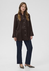Brown satin button-up shirt with long sleeves, a collar, and white buttons, paired with dark blue straight-leg jeans and striped heels.
