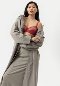 Grijze trenchcoat met brede mouwen over een rode met bloemen geborduurde beha. De rok is aansluitend met naaddetail. Gladde texturen aanwezig.