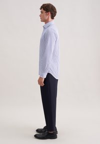 Camicia a maniche lunghe a righe azzurro chiaro e bianco con colletto classico, abbinata a pantaloni blu navy e scarpe nere. Texture liscia e vestibilità su misura.