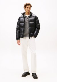 Black puffer jacket with a zippered front, ribbed cuffs, and an attached hood, layered over a grey cable-knit sweater and cream pants.