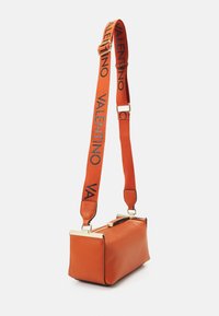 Sac à main en cuir orange avec une forme rectangulaire structurée. Dispose d'une bandoulière tissée ornée d'un logo et d'accents en métal doré.