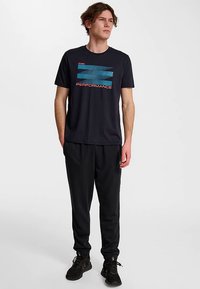 Zwart T-shirt met blauwe en rode tekst "PERFORMANCE," gecombineerd met zwarte sportbroek en zwarte sneakers. Eenvoudig, casual ontwerp.