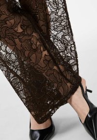 Brown floral lace fabric with intricate patterns and small sequins, paired with a smooth black heel shoe. Focus on texture and design details.