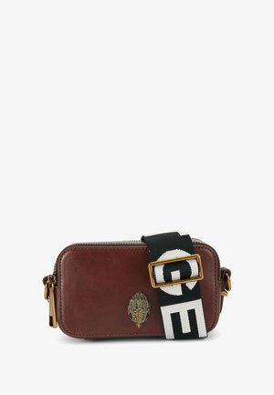 Bruine leren rechthoekige schoudertas met een decoratieve sluiting, een zwart-witte band met opvallende letters en een ritssluiting.