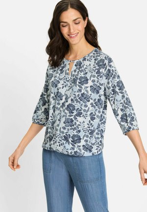 Hellbluse mit floralem Muster, die marineblaue Blumen und Blätter zeigt, kurze elastische Ärmel und einen Schlüsselloch-Ausschnitt hat. Kombiniert mit hellblauen Jeans.