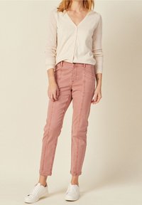 Ljusbeige cardigan med meshärmar, parat med rosa smala jeans med sömdetaljer, och vita sneakers.