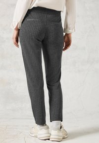 Pantalon gris à rayures fines avec une coupe ajustée, doté de deux poches arrière, porté avec des chaussettes blanches et des baskets beiges.