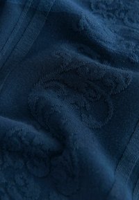 Dunkelblauer Stoff mit erhabenen floralen und Ranken gewebten Mustern und sichtbaren Nähten entlang der Kanten.