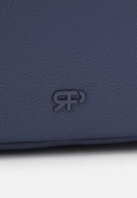 Borsa in pelle blu navy con superficie texturizzata; presenta un logo in rilievo nella parte inferiore. Forma compatta con linee pulite e design minimalista.