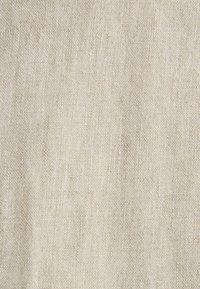 Tissu beige tissé avec une texture grossière et des fils entrelacés visibles créant une apparence de lin naturel.