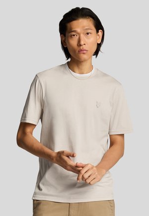 T-shirt beige chiaro a maniche corte, con scollo rotondo, in tessuto morbido, caratterizzato da un piccolo logo ricamato sul petto. Vestibilità casual.