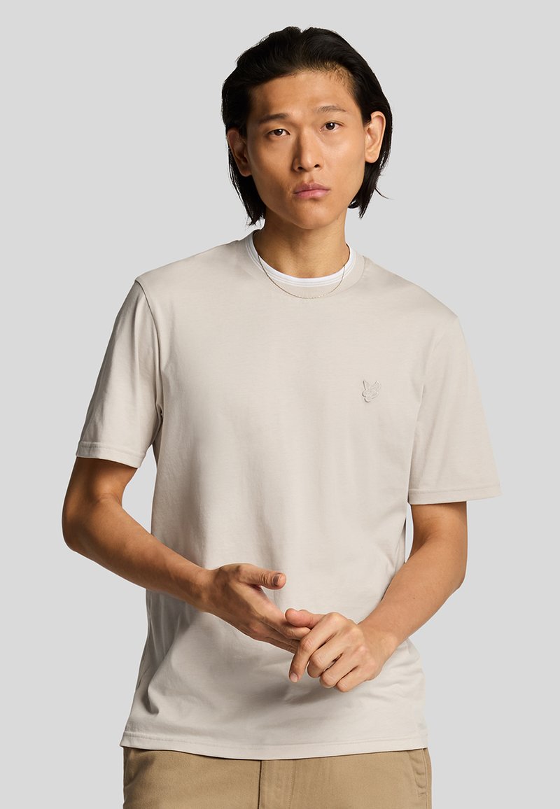 Helles beige T-Shirt mit kurzen Ärmeln, Rundhalsausschnitt, aus weichem Stoff, mit einem kleinen gestickten Logo auf der Brust. Lässige Passform.