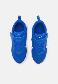 Une paire de baskets Nike bleues pour enfants avec des logos swoosh blancs, en tissu en maille, des bandes Velcro et des languettes de traction, vues du dessus sur un fond blanc.