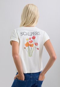Camiseta de algodón blanca de manga corta, con el texto "SCALPERS" y un colorido estampado floral en la parte trasera con flores rosas y amarillas.