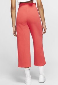 Korallröda ribbade vida byxor med hög midja, som har en slät yta och kort längd, i kombination med vita sneakers och strumpor.