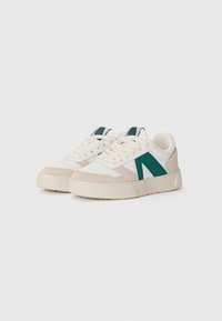 Sneakers con tomaia in pelle bianca, accenti in suede verde e beige, punta rotonda, lacci piatti e suola in gomma testurizzata.