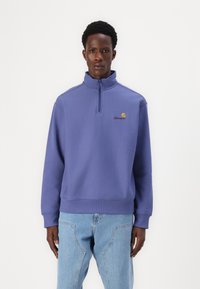 Purple sweatshirt with a high collar and half-zip design. Features a small embroidered logo on the chest and ribbed cuffs. Extended hem.