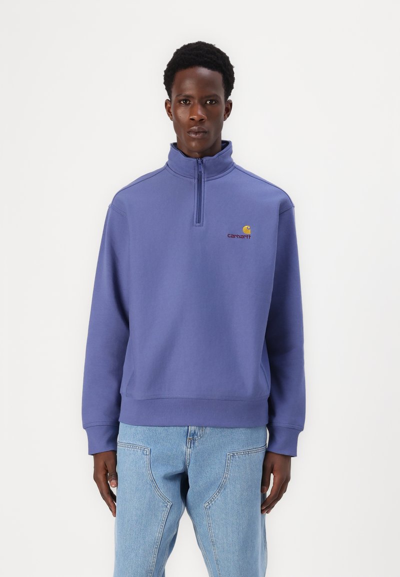 Purple sweatshirt with a high collar and half-zip design. Features a small embroidered logo on the chest and ribbed cuffs. Extended hem.