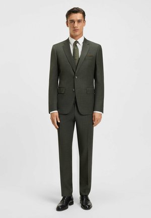 Dark green tailored suit featuring a textured fabric, single-breasted jacket, notch lapels, and paired with a white shirt and patterned tie.