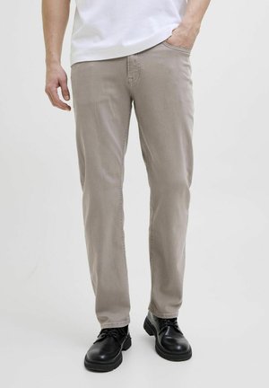 Pantalons en coton beige avec une coupe droite, texture subtile et poches avant, associés à des chaussures noires à lacets.
